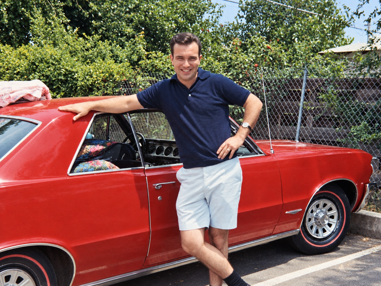 Andre smiling beside his red classic coupe outdoors